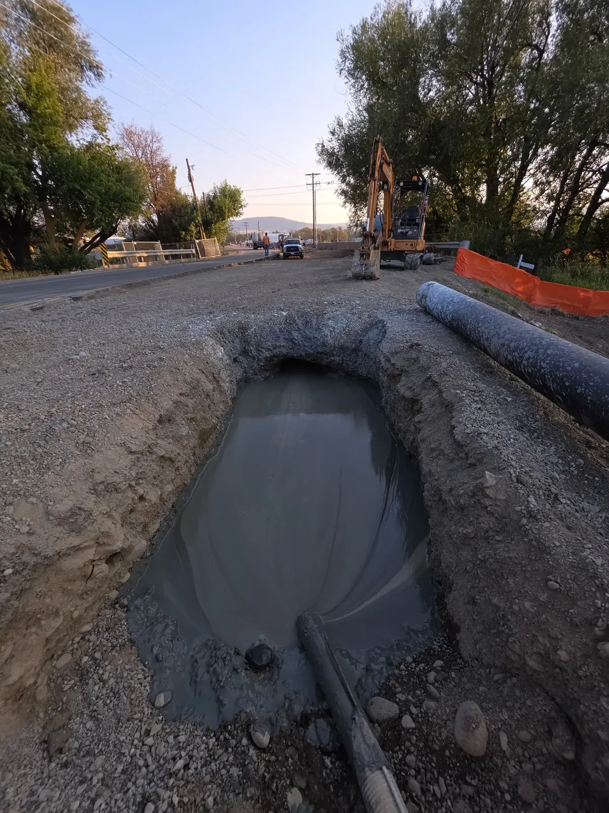 Open excavation with vacuum hose alongside a paved road